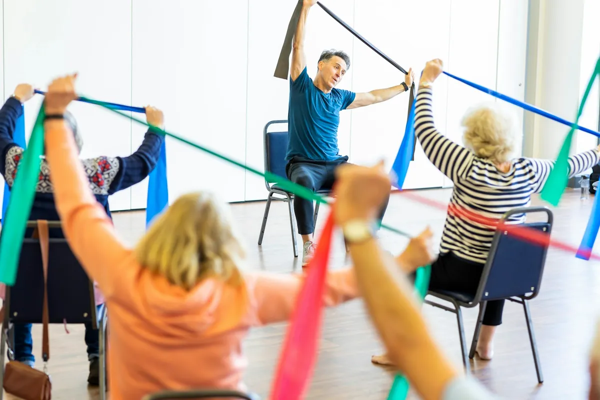 An instructor leads a bright studio class of adults using resistance bands.